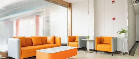 A modern hotel lobby with a large window, orange sofas, a marble coffee table, and a small round table with a plant.