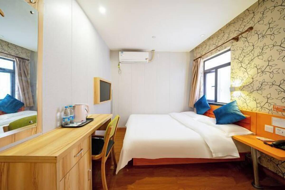 A hotel room with a bed, a desk, a chair, a mirror, and a window.