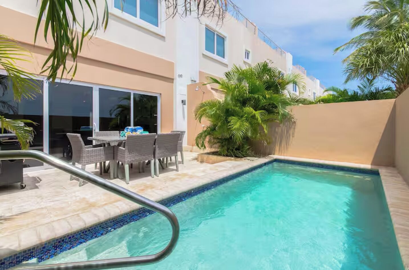 A swimming pool with a tiled edge, surrounded by a patio area with outdoor furniture and palm trees.