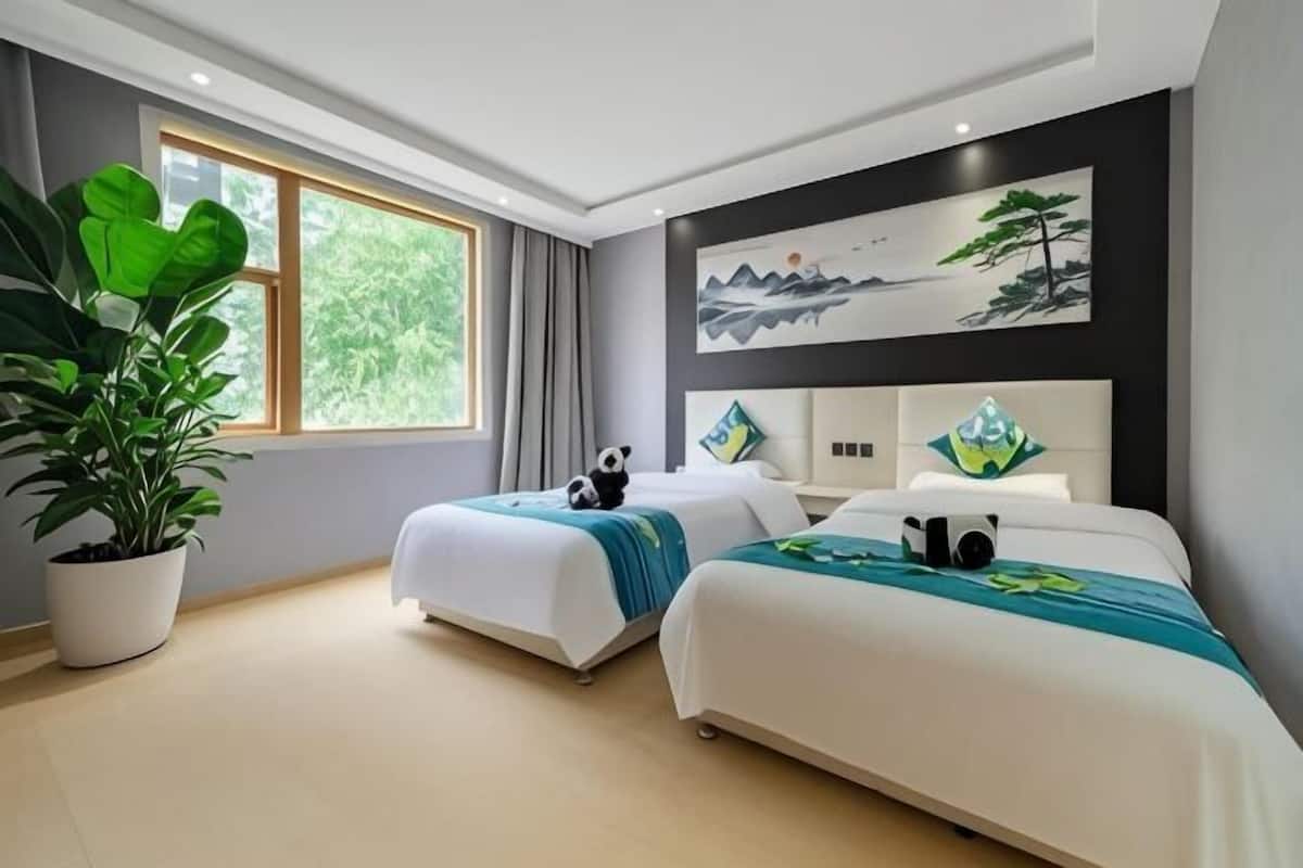 Una habitación de hotel moderna con dos camas, un ventanal grande y una planta en maceta.