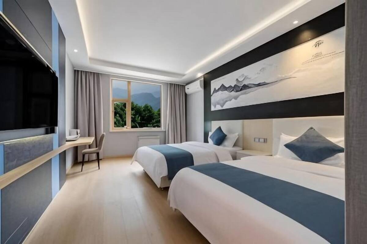 Habitación de hotel con dos camas, un escritorio, un televisor y un amplio ventanal con vista a la montaña.