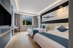 Habitación de hotel con dos camas, un escritorio, un televisor y un amplio ventanal con vista a la montaña.