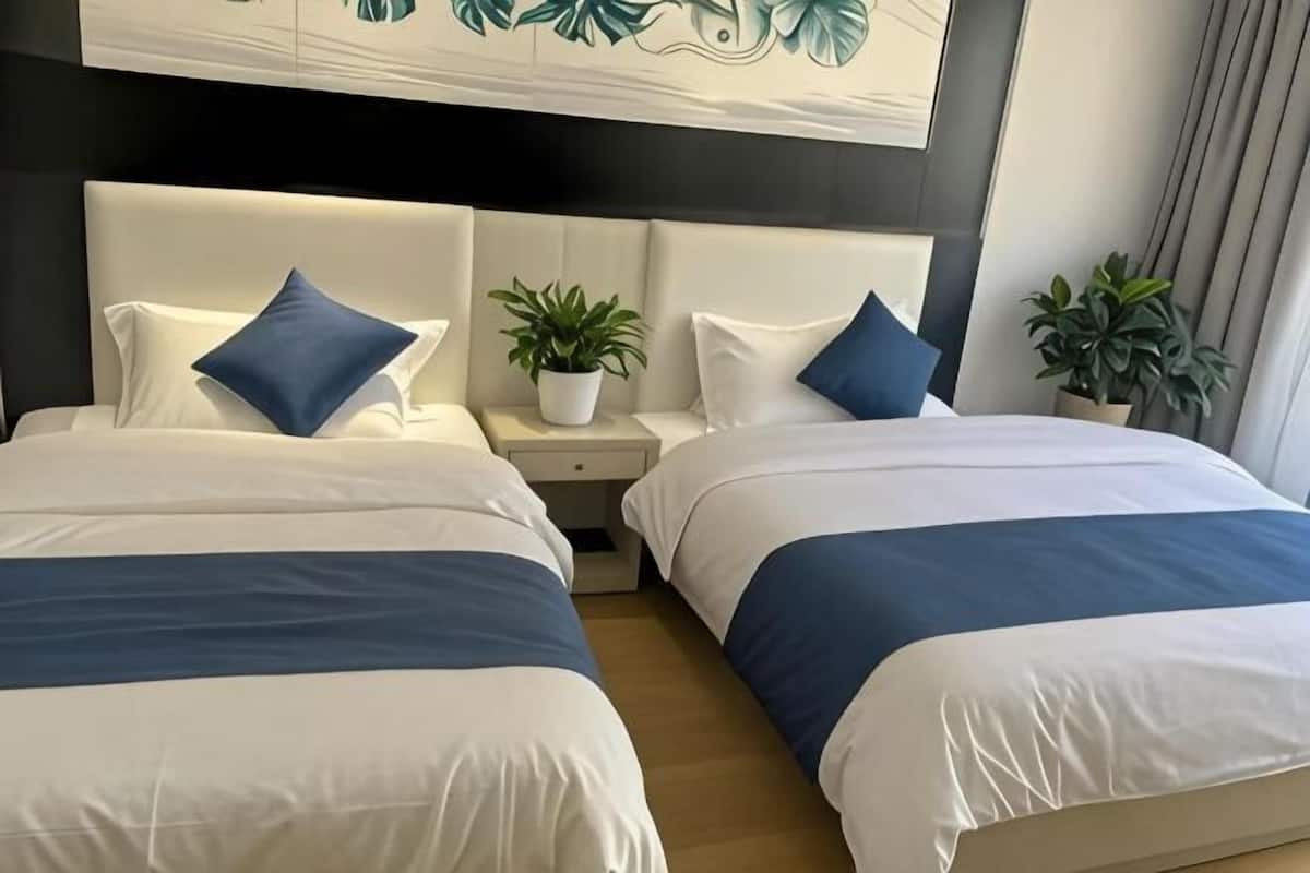 Habitación de hotel con dos camas, cada una con cabecera, mesita de noche y planta en maceta.