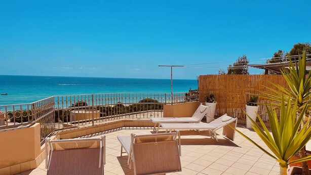 A sunlit outdoor seating area with lounge chairs and a view of the sea. - Bright penthouse in Costa Rei - Sea view and relaxing atmosphere (Costa Rei)