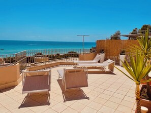 A sunlit outdoor seating area with lounge chairs and a view of the sea. - Bright penthouse in Costa Rei—Sea view and a relaxing atmosphere (Costa Rei)