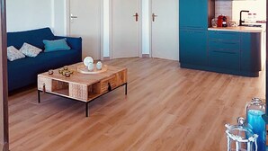A modern apartment with a wooden floor, a blue sofa, a coffee table, and a kitchen area with cabinets. - Bright penthouse in Costa Rei - Sea view and relaxing atmosphere (Costa Rei)