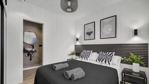 Une chambre moderne avec un grand lit, deux tables de chevet, une commode, une lampe fixée au mur et un miroir.