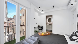 Une chambre d’hôtel moderne avec un balcon, un lit agrémenté d’un plateau de petit-déjeuner, un bureau et une salle de bain dotée d’un miroir rond.