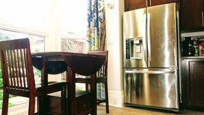 Une cuisine équipée d’un réfrigérateur en acier inoxydable, d’une table à manger avec des chaises et d’une fenêtre avec des rideaux.