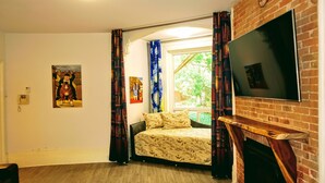 Une chambre à coucher avec un lit, un téléviseur fixé au mur en briques, une fenêtre avec des rideaux et un tableau accroché au mur.