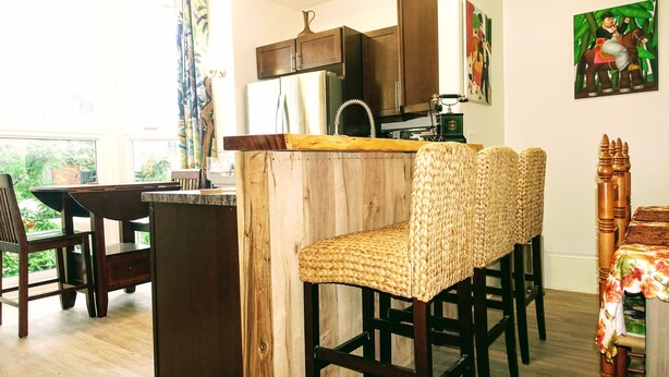 Une cuisine avec des tabourets de bar en bois, un réfrigérateur et une fenêtre avec des rideaux.
