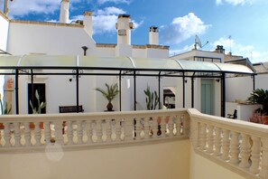 Un espace extérieur abrité, doté d’une balustrade, de plantes en pot et d’un bâtiment aux murs blancs et aux cheminées.