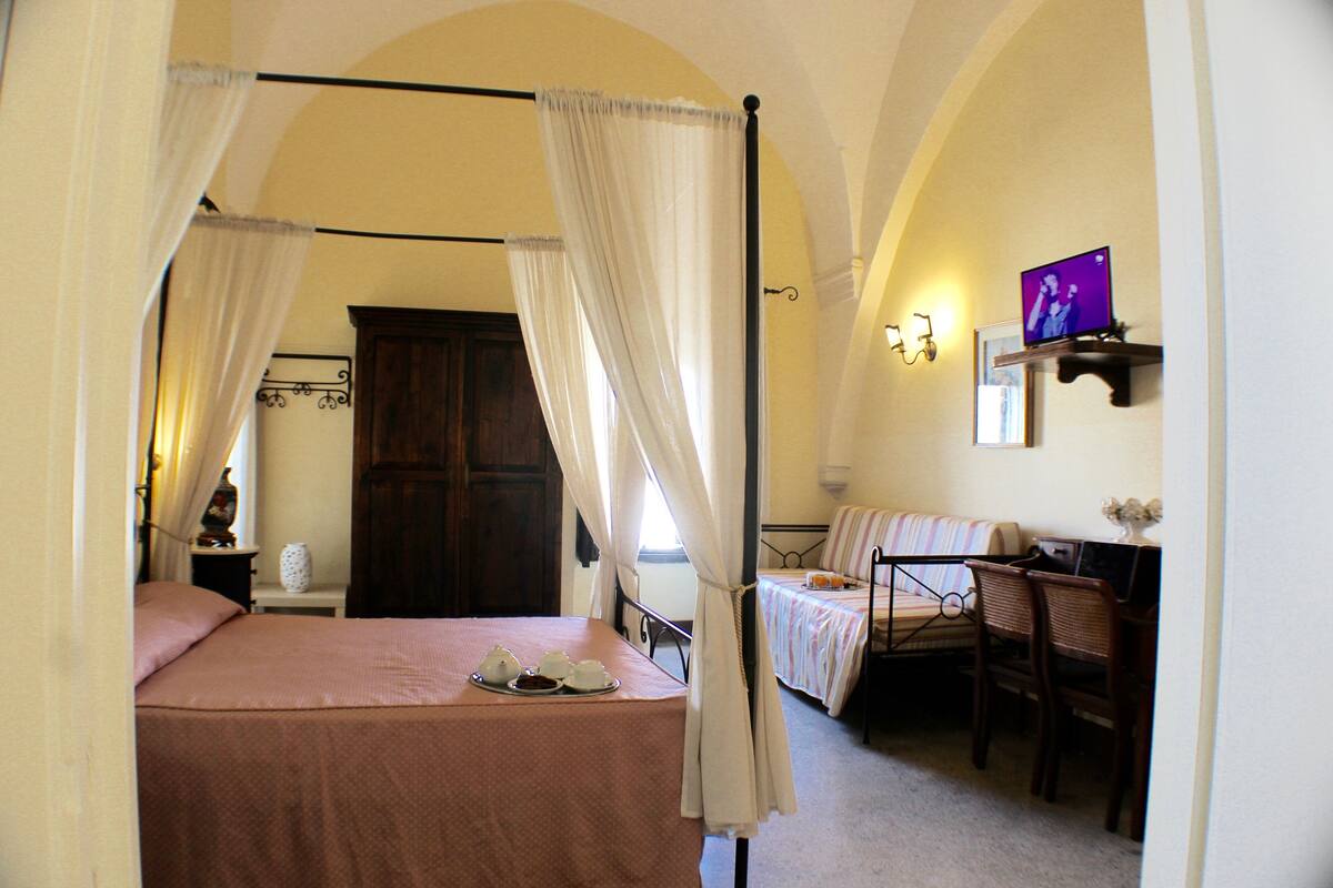 Ein Schlafzimmer mit Himmelbett, Schreibtisch mit Stuhl und einem an der Wand befestigten Fernseher.