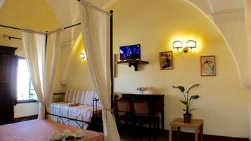 A bedroom with a four-poster bed, a desk with a chair, a small table with a potted plant, and wall-mounted lights.