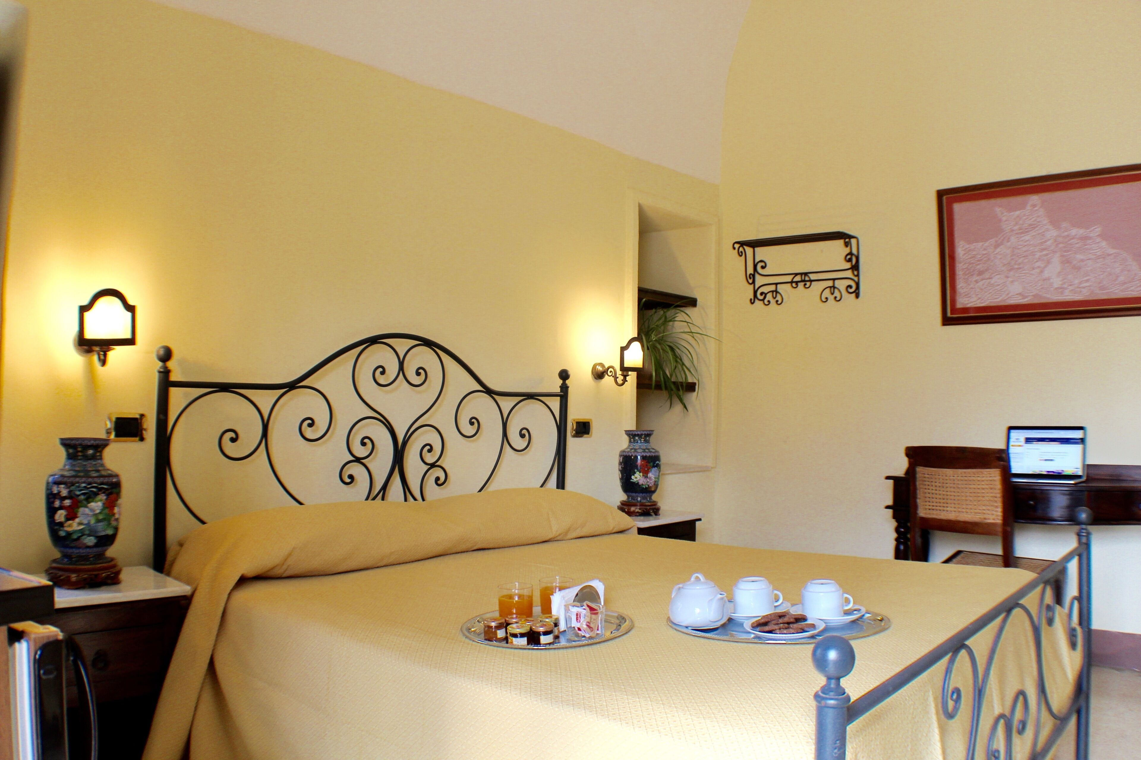 A neatly made bed with a tray of breakfast items, a laptop on a desk, and a framed picture on the wall.