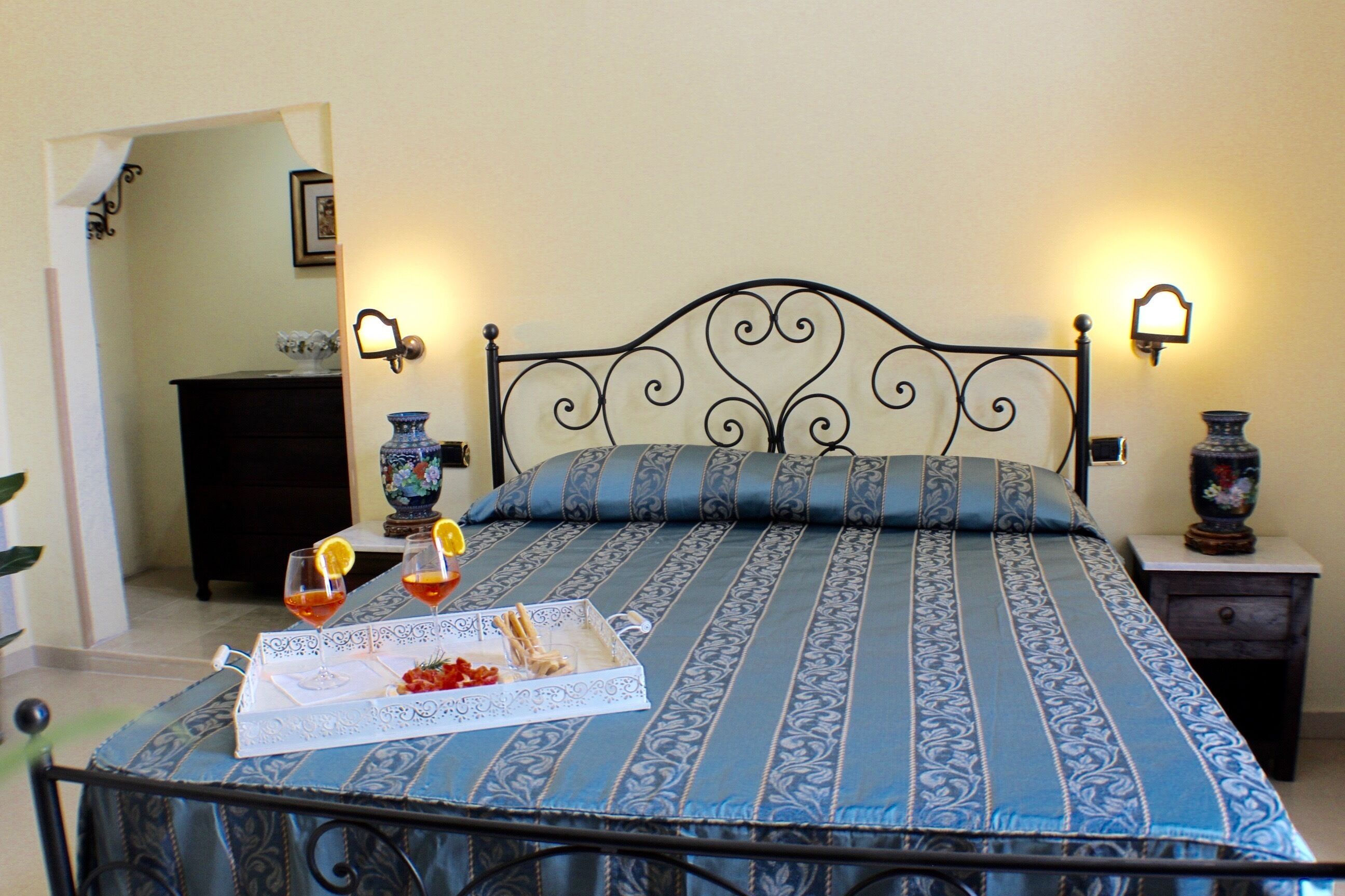 Un lit bien fait, recouvert d’une couvre-lit à motifs bleus et blancs, avec deux lampes de chevet et un plateau contenant des collations et des boissons, posé sur le lit.