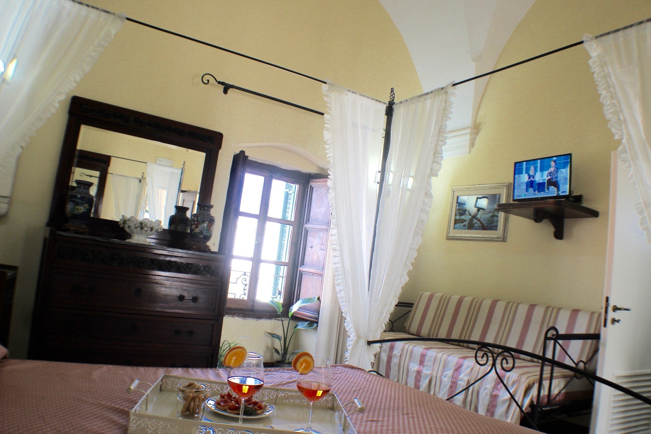A bedroom with a bed, a dresser, a mirror, a television, and a window with curtains.