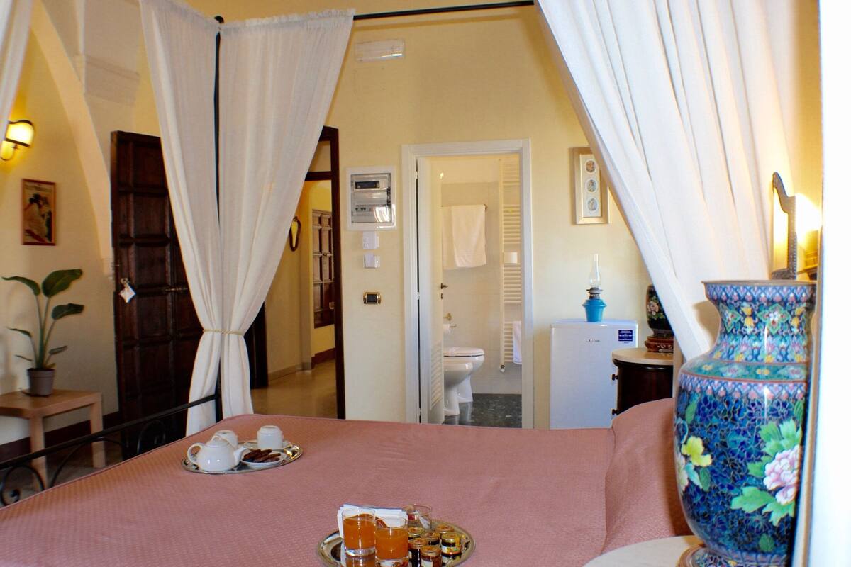 Ein Hotelzimmer mit Bett, einem Frühstücksbrett, einer Vase und einem durchgegangenen Tür erkennbaren Badezimmer.