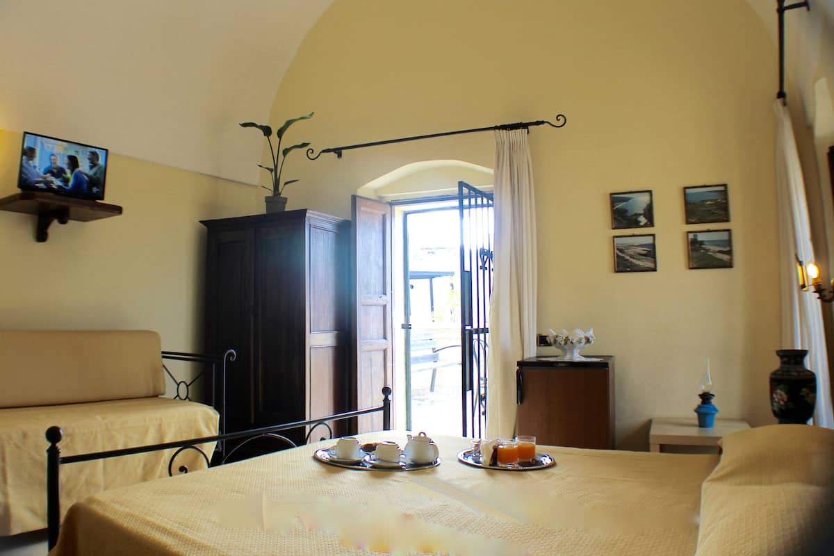 Ein Zimmer mit zwei Betten, einem Esstisch mit Frühstücksangeboten, einem Fernseher und Blick ins Freie.