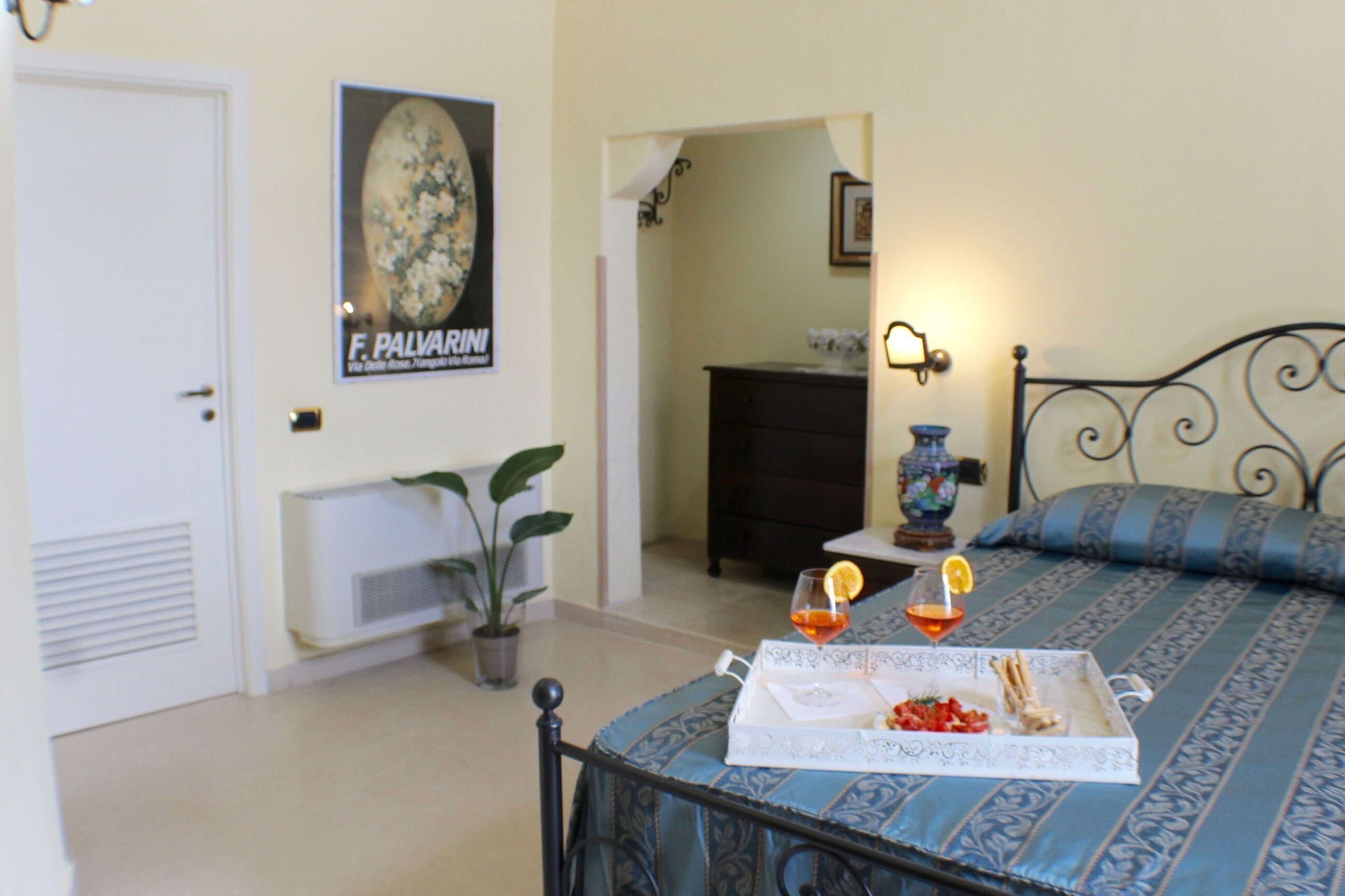 A bedroom with a bed, a bedside table with a lamp, a potted plant, and a poster on the wall.