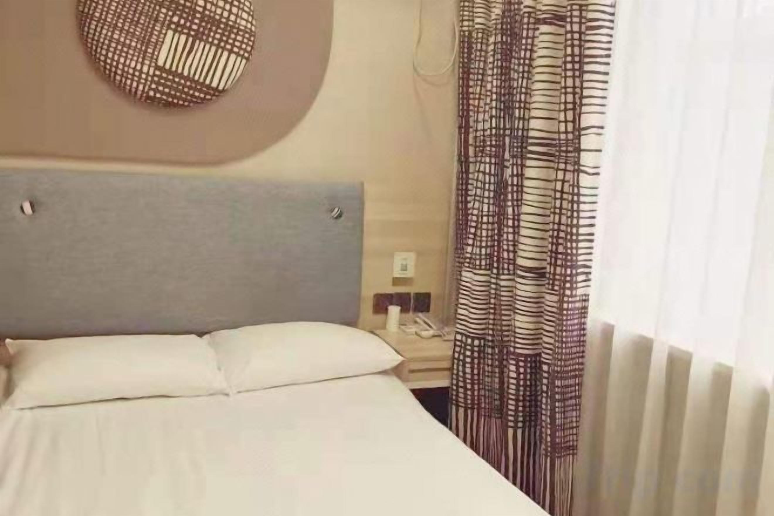 A hotel room with a bed, a bedside table, a telephone, and a window with curtains.