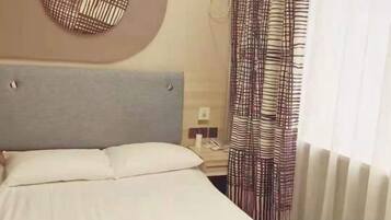 A hotel room with a bed, a bedside table, a telephone, and a window with curtains.