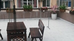 An outdoor seating area with a wooden table and bench, surrounded by potted plants and a concrete floor.