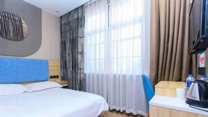 A hotel room with a bed, a desk with a kettle, curtains, and a television.