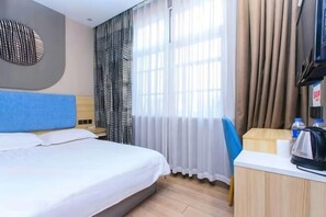 Une chambre d’hôtel équipée d’un lit, d’un bureau avec une bouilloire, de rideaux et d’un téléviseur.