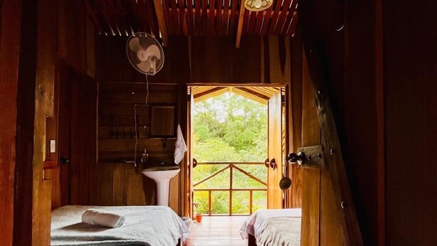Une cabane en bois avec deux lits, un ventilateur et une vue sur la verdure environnante.
