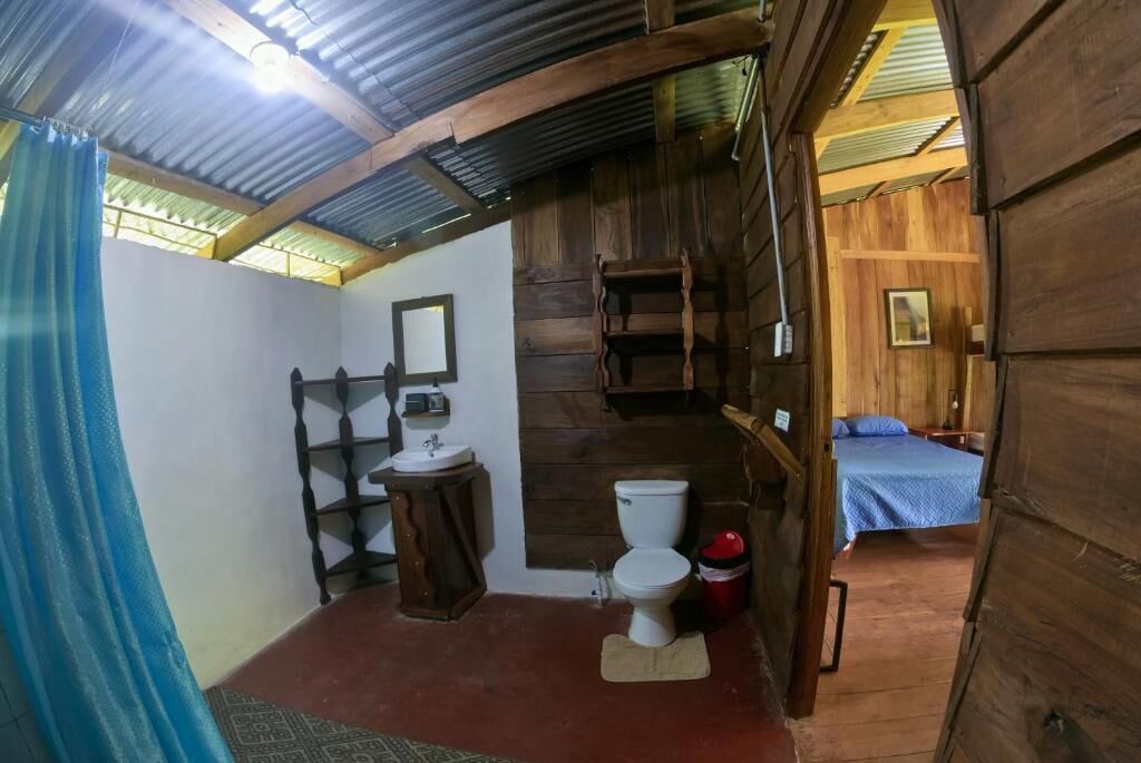 A rustic wooden cabin with a bathroom featuring a toilet, sink, and wooden shelves.