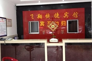 A reception desk with a red wall featuring Chinese characters and a decorative emblem. - Feixiang Express Inn (Tongcheng)
