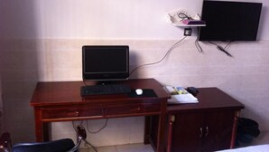 A hotel room with a wooden desk, a computer, a TV mounted on the wall, and a chair. - Feixiang Express Inn (Tongcheng)