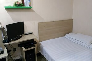 A bedroom with a bed, a desk with a computer, and a shelf with a plant. - Feixiang Express Inn (Tongcheng)