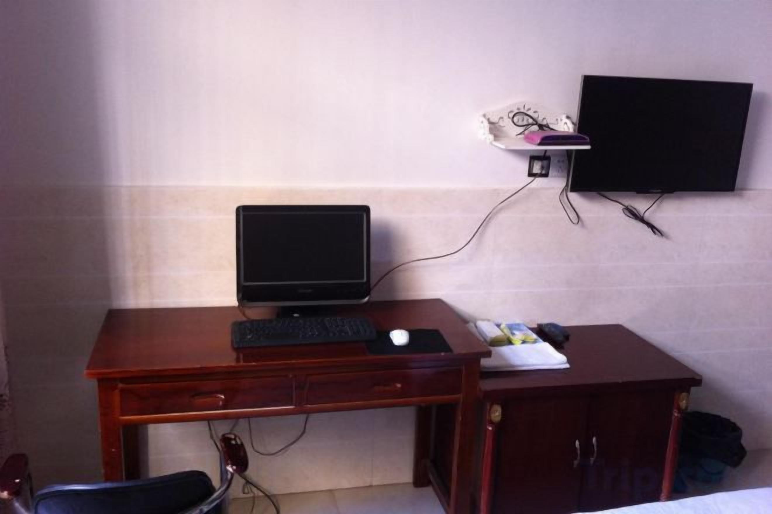 A hotel room with a wooden desk, a computer, a flat-screen TV, and a bed.