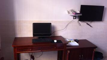 A hotel room with a wooden desk, a computer, a flat-screen TV, and a bed.