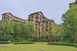 Un edificio residencial de varios pisos con balcones, rodeado de follaje cuidado y un cielo despejado.