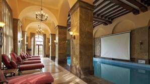 Eine großzügige Lobby mit Pool, roten Liegestühlen, Marmorsäulen und einem Kronleuchter.