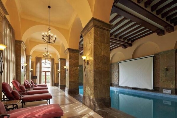 Un vestíbulo amplio con piscina, sillones rojos de descanso, columnas de mármol y un candelabro.