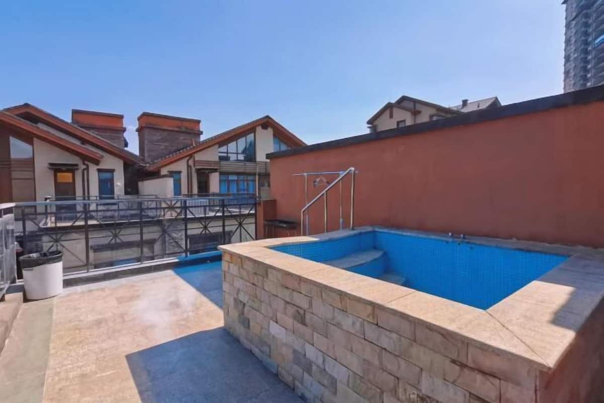 Una piscina al terrat amb mur de pedra, barana metàl·lica i cel blau clar.
