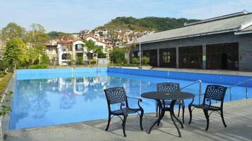 A swimming pool with chairs and a table, surrounded by buildings and greenery.