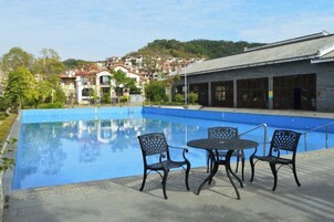 Una piscina con sillas y una mesa, rodeada de edificios y vegetación.