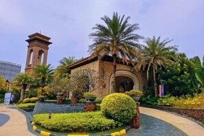 Un bâtiment doté d’un clocher, entouré de jardins bien entretenus et de palmiers.