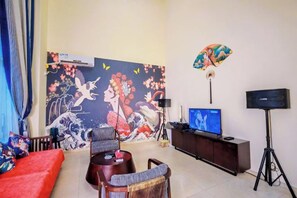 Una sala de estar con televisor, sofá, mesa de centro y un mural en la pared.