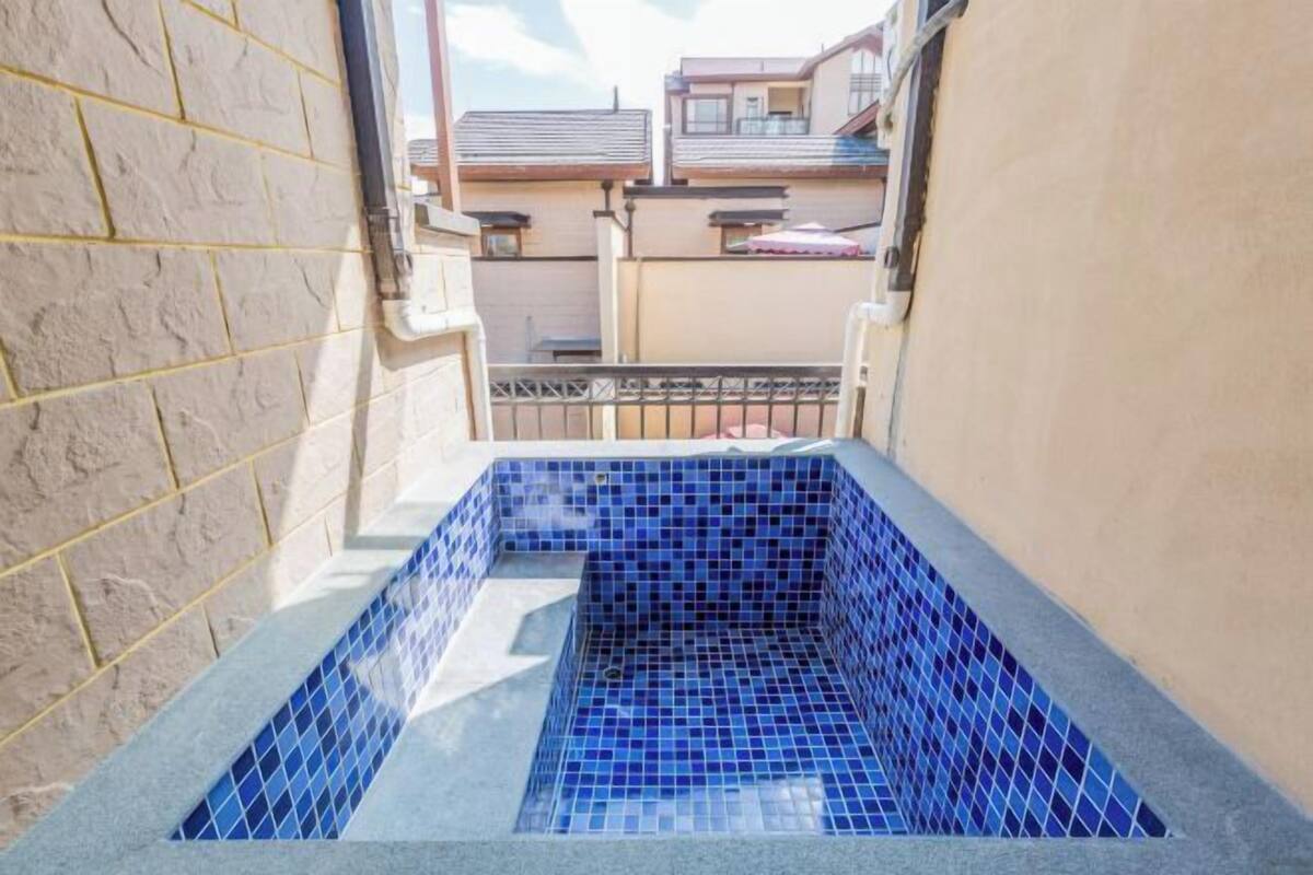 Una piscina petita i tancada amb mosaic blau, envoltada per una paret de pedra i una barana metàl·lica.