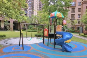 Ein Spielplatz mit Rutsche und Schaukeln, umgeben von Grünflächen und Wohngebäuden.