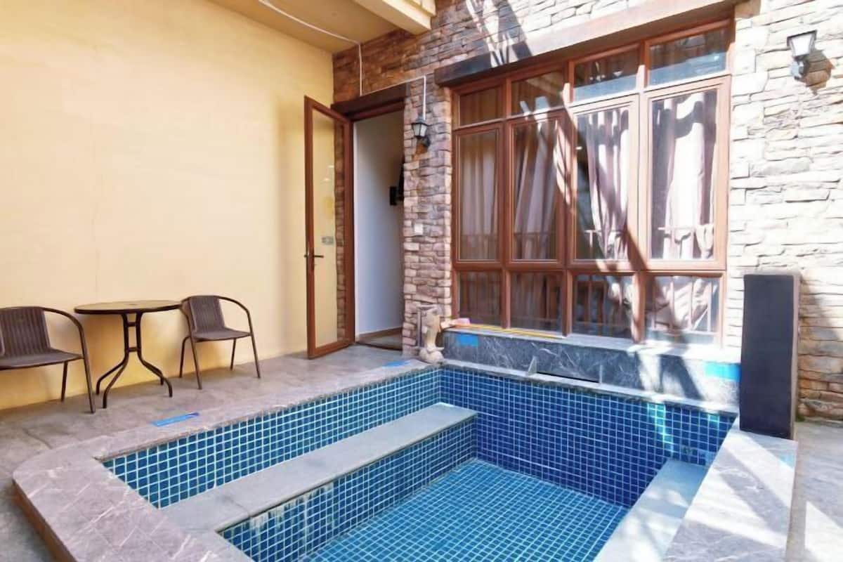 Una piscina petita a l'exterior amb parets de pedra i una finestra. Hi ha dues cadires i un taulell a prop.