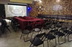Un salón de conferencias con una larga mesa cubierta con mantel rojo, rodeada de sillas y una pantalla de proyección al fondo.