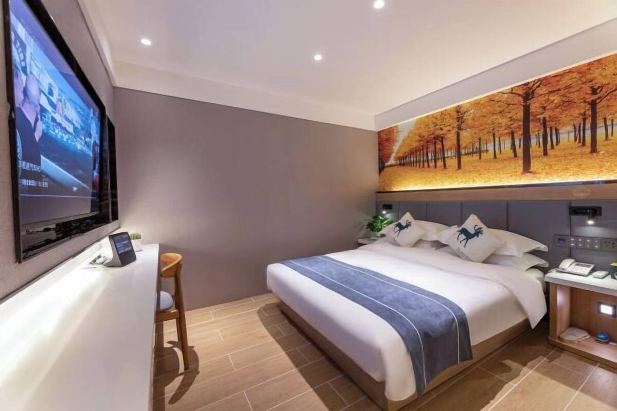 Una camera d'albergo con un letto, una scrivania, una televisione e un'opera d'arte raffigurante alberi.