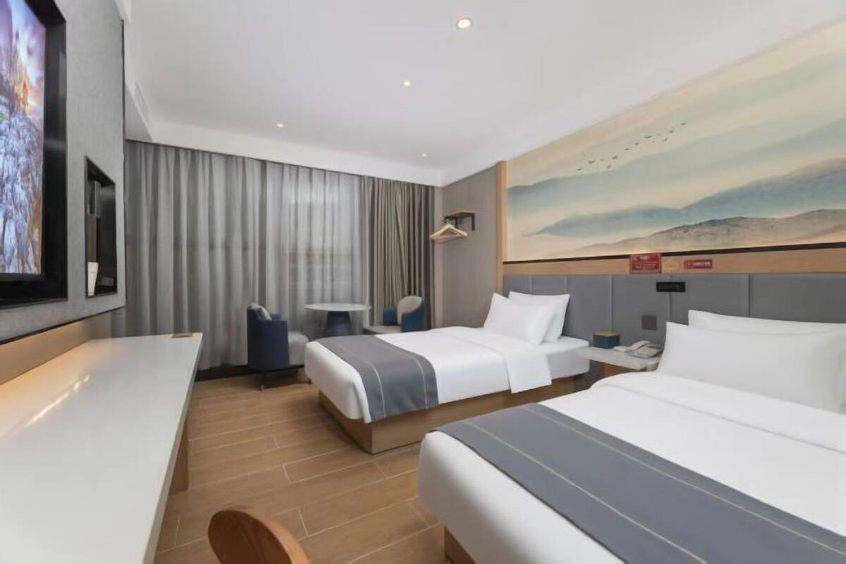 Una camera d'albergo con due letti, una scrivania, una sedia, una TV e un quadro appeso al muro.